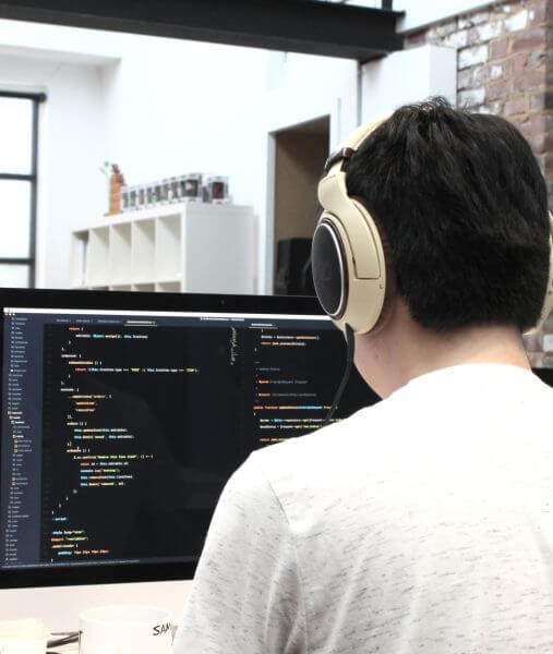 Back of man wearing headphones looking at computer working on cloud and IOT services