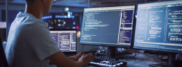 Man looking at multiple desktop computer screens typing as he works on solving technology solutions