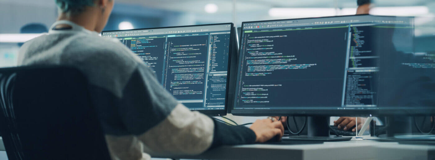 Back of developer looking at two computer screens working on cloud cost optimization