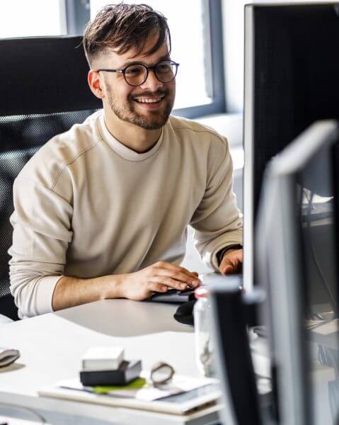 Man smiling while sitting at desk looking at computer for devops and it